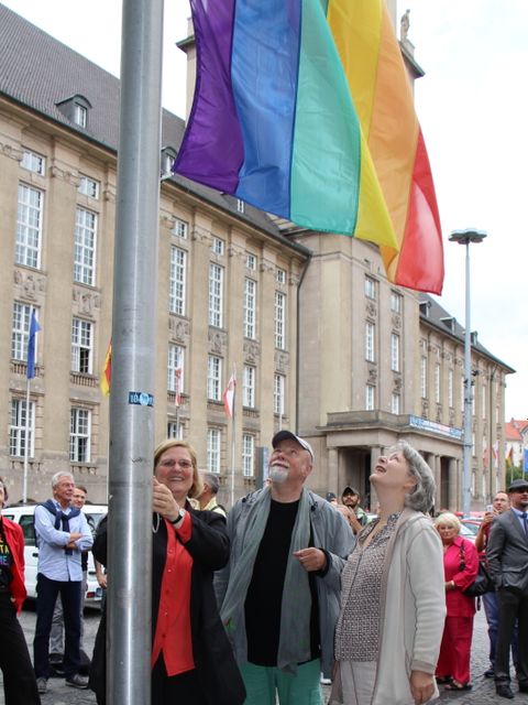 Bildvergrößerung: Bezirksbürgermeisterin Angelika Schöttler (l.) hisst die Regenbogenfahne unter den prüfenden Blicken von Dr. Elisabeth Ziemer (r.) und Gerhard Hoffmann (m.)