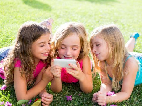 drei Mädchen liegen auf einer Wiese und sehen in ein Handy