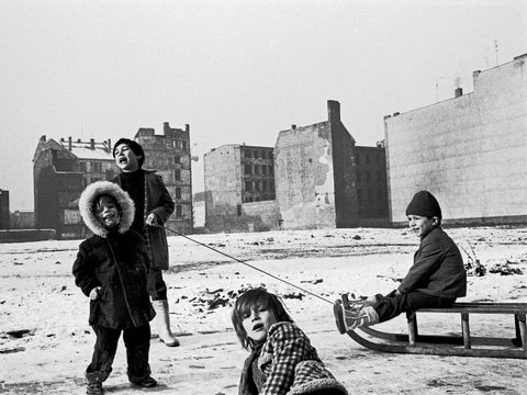 Bildvergrößerung: Eine schwarz-weiß Fotografie von 4 Kindern mit einem Schlitten auf einen Freifläche mit Schnee.