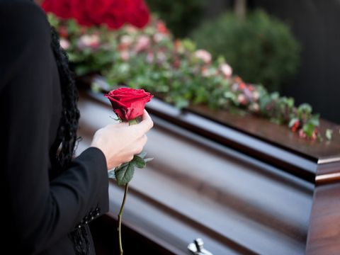 Frau steht auf einer Beerdigung mit Rose in der Hand vor einem Sarg