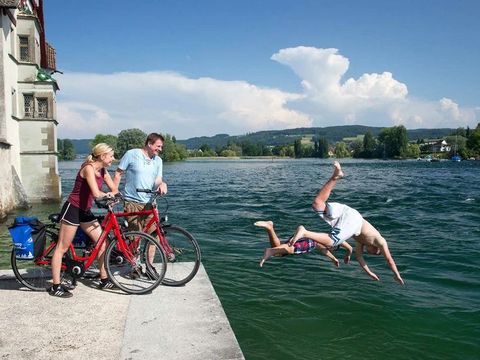 Zwei Radfahrer am Bodensee schauen zu wie zwei Menschen von einer Mauer in den See springen