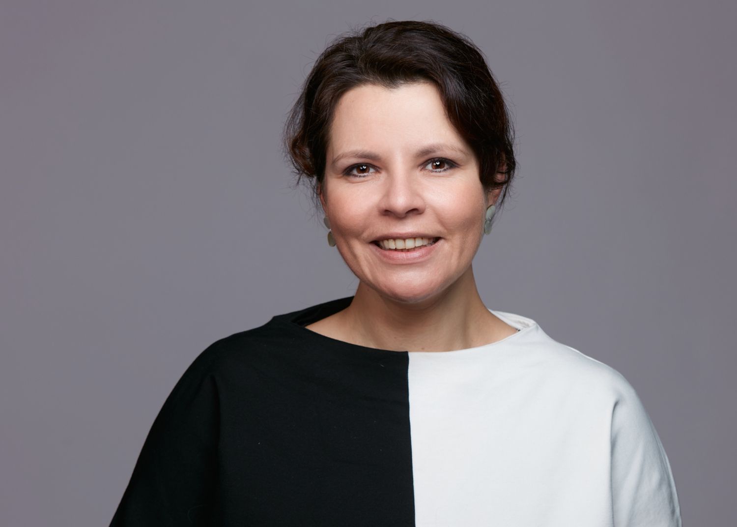 Marcia Schranner im Profil vor grauem Hintergrund mit schwarz-weißem Oberteil