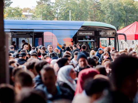 Eine große Gruppe von Menschen steht vor dem Karrierebus des Landes Berlin. Interessierte lassen sich zu Ausbildung und Einstieg beraten. Standort des Busses ist vor dem Berliner Olympiastadion. 
