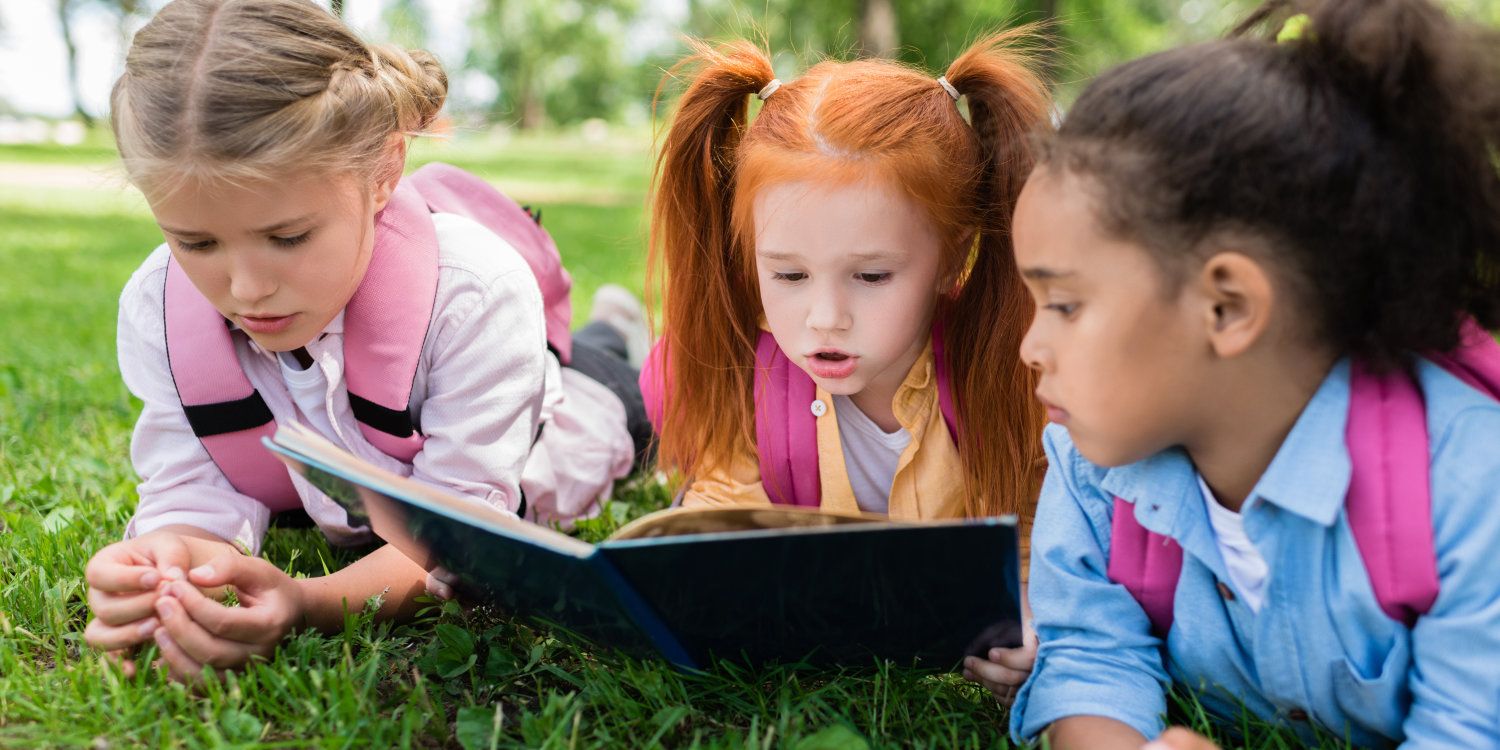 Drei Kinder lesen im Park auf der Wiese gemeinsam ein Buch