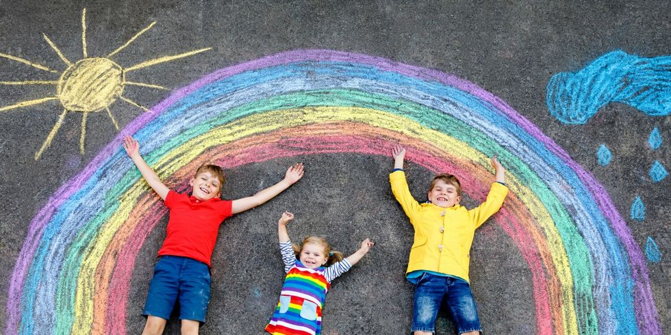 Kinder mit Malerei eines Regenbogens auf der Straße liegend