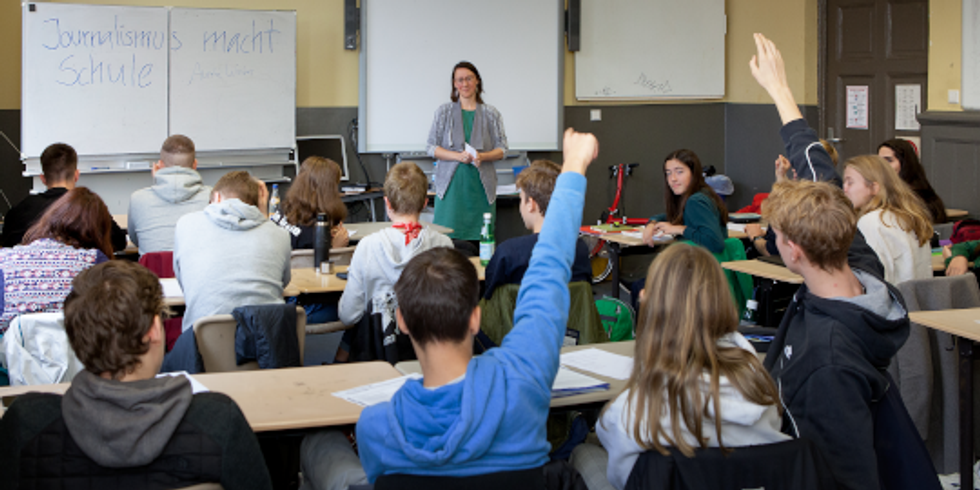 Schulklasse in einem Unterrichtsraum stellt Fragen an eine Journalistin