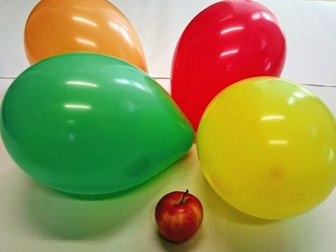 Ein Apfel umgeben von 4 bunten Luftballons