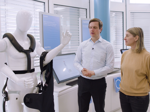 Ein Mannequin, ausgestattet mit Tech-Gegenständen, ein Mitarbeiter des Projekts und eine weitere Person stehen im Industrie 4.0 Labor.