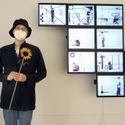 Bildvergrößerung: Hyunho Park vor ihrem Werk: Time Crystals - Neun Räume, 2019, BU: Hyunho Park: Time Crystals - Neun Räume, 2019 Auf der rechten Seite des Bildes hängen 9 Monitore an der Wand .