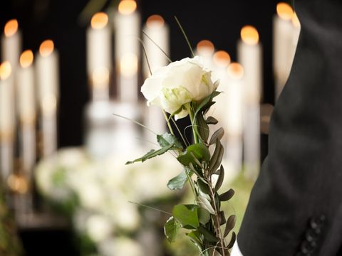 Ein schwarz bekleideter Männerarm hält eine weiße Rose bei einer Trauerfeier