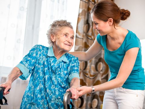 Junge Pflegerin betreut ältere Dame an Gehhilfe