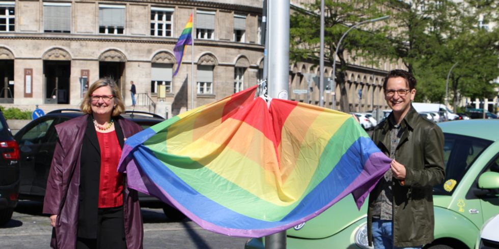 Eine Frau und eine Mann halten eine Fahne in den farben des Regenbogens