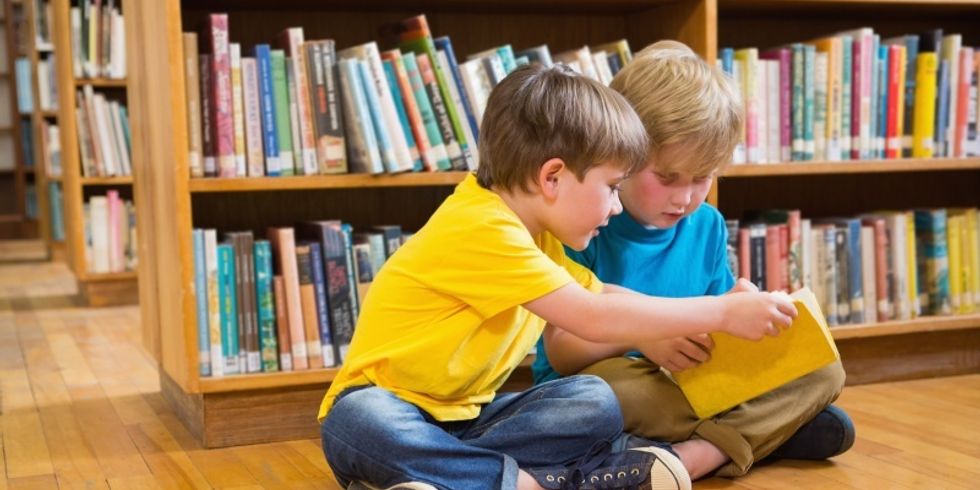 zwei Jungs sitzen vor einem Bücherregal und lesen in einem Buch