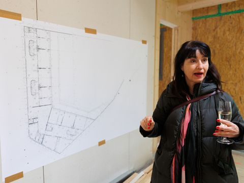 Architektin Laura Fogarasi-Ludloff steht gestikulierend vor dem Grundriss-Plan des Kindergartens
