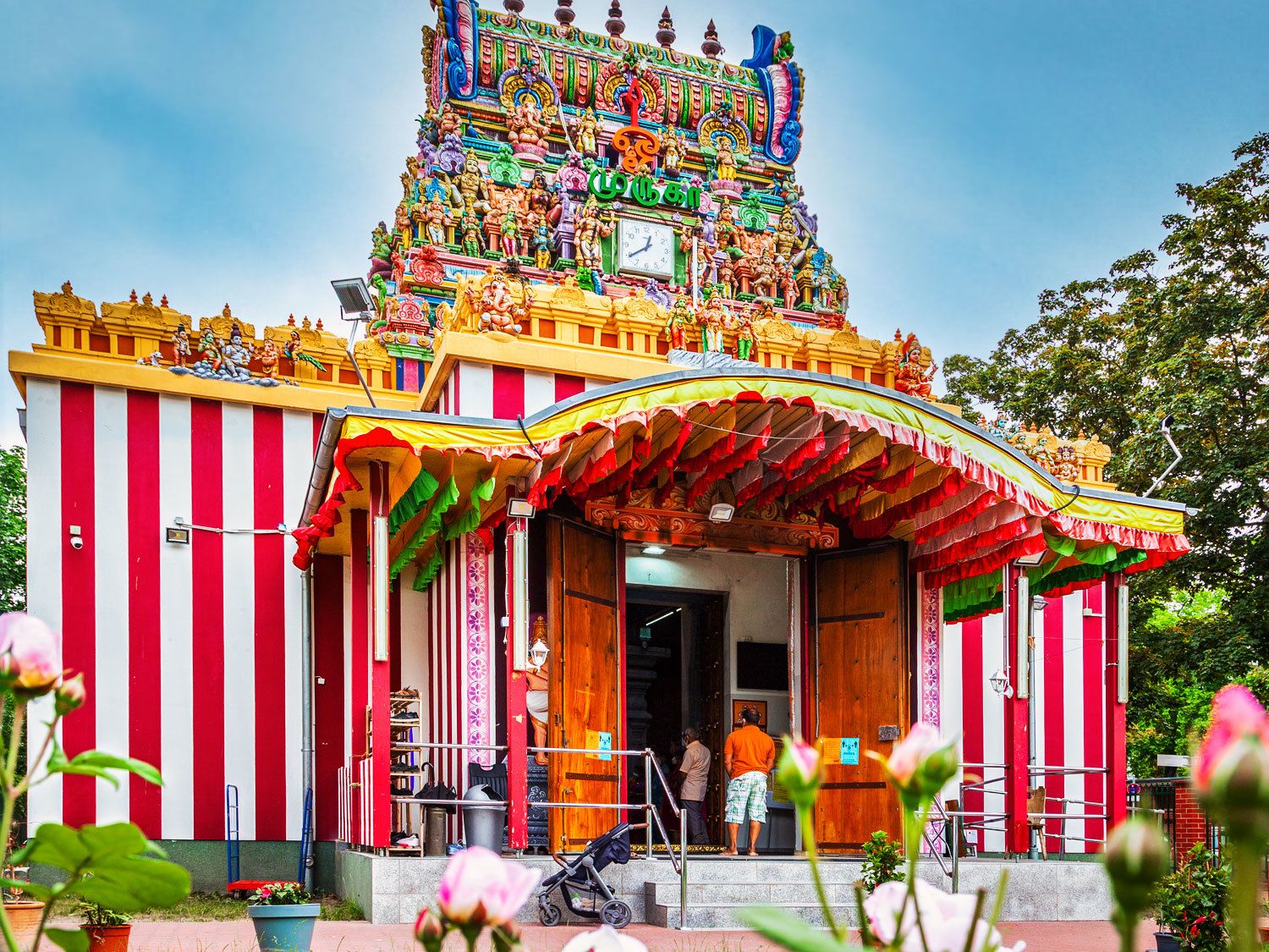 Ein Hindutempel. Der unterer Teil des Tempels ist rot-weiß gestreift gestrichen. Darüber eine Art Turm mit vielen hinduistischen Göttern. Die Götter sind sehr farbenfroh angemalt. 