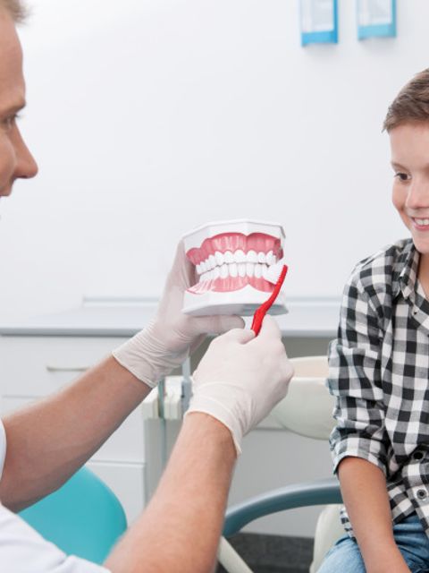 Zahnarzt erklärt Jungen anhand eines Modells die richtige Zahnpflege