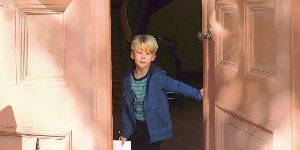 Ein kleiner Junge steht in der offenen Tür und hat ein Blatt Papier in der Hand.
