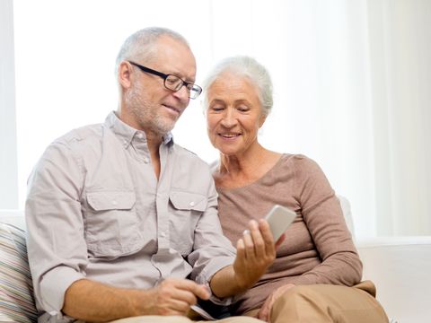 Ein älteres Ehepaar sitzt auf einem Sofa und hantiert mit einem Smartphone