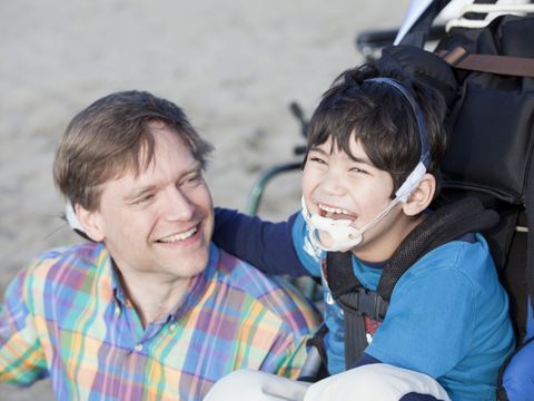 Ein Vater sitzt lächelnd neben seinem behinderten Sohn am Strand
