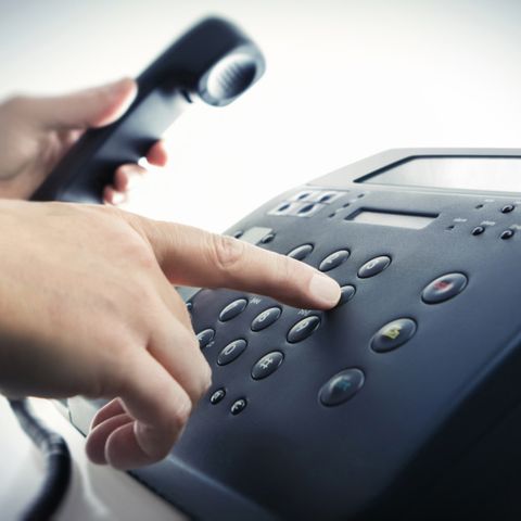 Eine Hand wählt eine Rufnummer auf dem Telefon