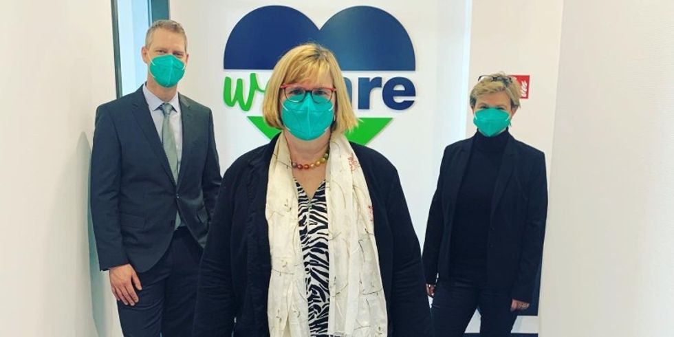 Drei Personen mit Mund-Nase-Masken stehen in einem Flur