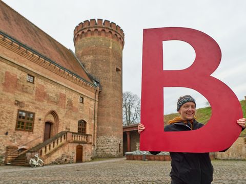 Bildvergrößerung: Junge Frau mit einem großen B als Buchstabenschild vor dem Juliusturm auf der Zitadelle