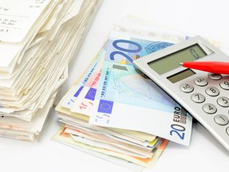 Das Bild zeigt einen Rechnungs- und einen Geldstapel mit Taschenrechner und Stift