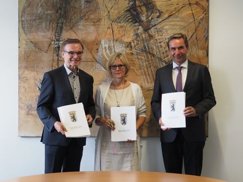 Die drei Behördenchefs stehen mit dem unterzeichneten Kooperationsvertrag vor einem Gemälde. 