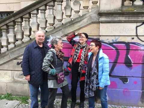 Vier lachende Personen im beginnenden Rentenalter vor einer Graffiti-besprühten Treppe