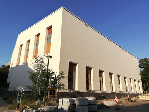 Ansicht der beigefarbenen Fassade der neuen Sporthalle vor blauem Himmel