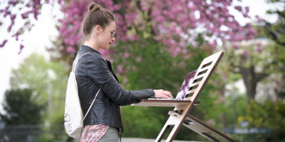 Frau steht im Park und arbeitet an Laptop