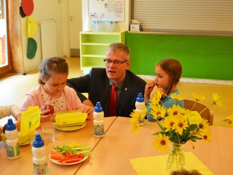 Bildvergrößerung: Bezirksbürgermeister Heltmur Kleebank mit Erstklässlerinnen die gerade eine Brotbox erhalten haben am Tisch