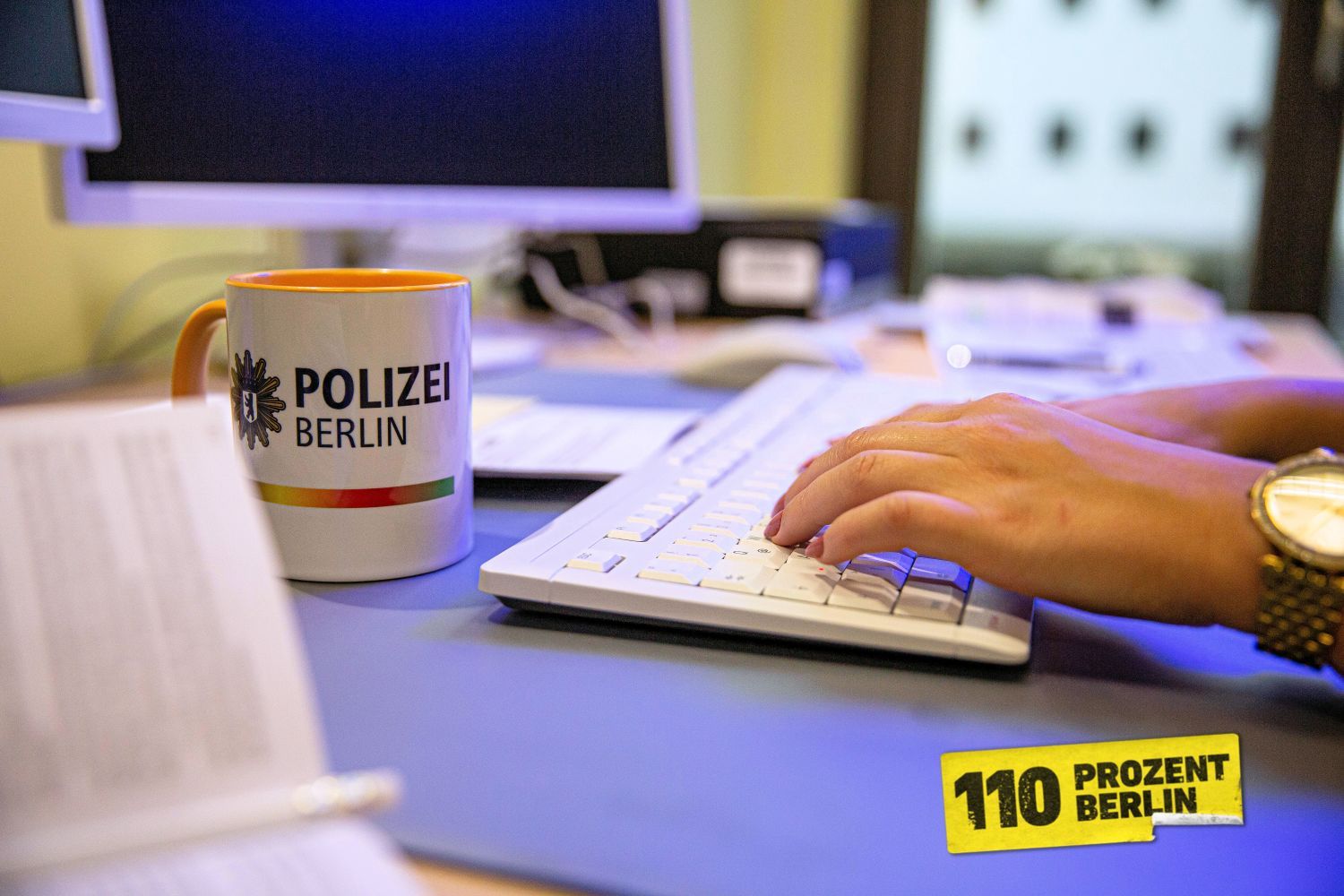 Hände auf einer Tastatur, davor eine Tasse mit Word-Bild-Marke Polizei BErlin