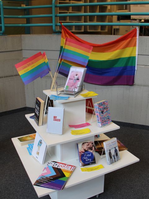 Bildvergrößerung: Ein Tisch mit Büchern sowie Fahnen in den Farben des Regenbogens