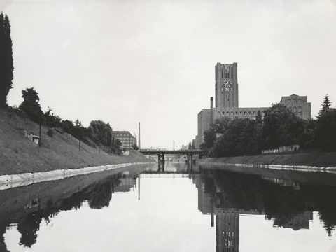 Bildvergrößerung: Eine schwarz-weiß Fotografie von einem Fuss. An einem Flussufer ist ein großes gebäude mit Turm.