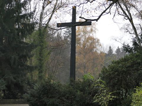 Bildvergrößerung: Ein mehrere Meter hohes Holzkreuz umgeben von Bäumen und Büschen.