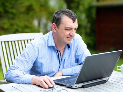Mann sitzt im Garten vor dem Laptop und arbeitet von zu Hause