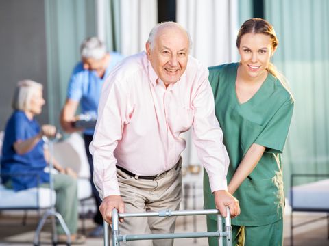 Eine junge Pflegerin hilft einem ältern Herren am Gehgestell