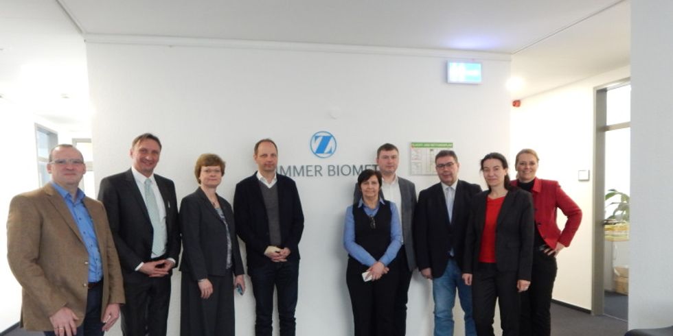 Gruppenbild vor dem Zimmer-Biomet Logo mit Bezirksbürgermeisterin Cerstin Richter-Kotowski, Unternehmen Zimmer-Biomet, Wirtschaftsförderung Steglitz-Zehlendorf