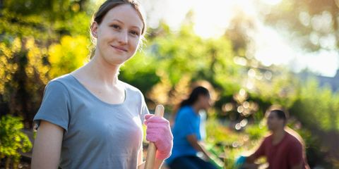 Portrait of Caucasian young woman student working to cleanup community garden neighborhood park area in residential district with youth organization volunteer charity crew in summer