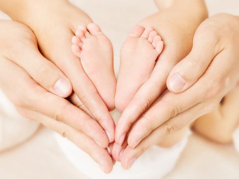 Die Füße eines Neugeborenen werden von den Händen der Eltern umrahmt. Die Hände bilden ein Herz.