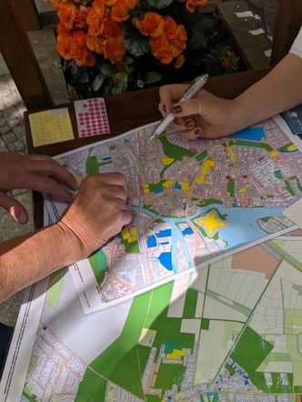 Zwei Personen markieren auf einem Stadtplan verschiedene Stellen mit Stiften und Aufklebern.