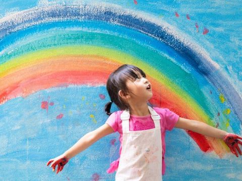 Ein Kind steht vor einem gemalten Regenbogen