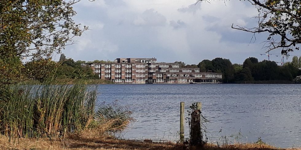 Hinter einem See ist ein großes vierstöckiges Gebäude direkt am Ufer.