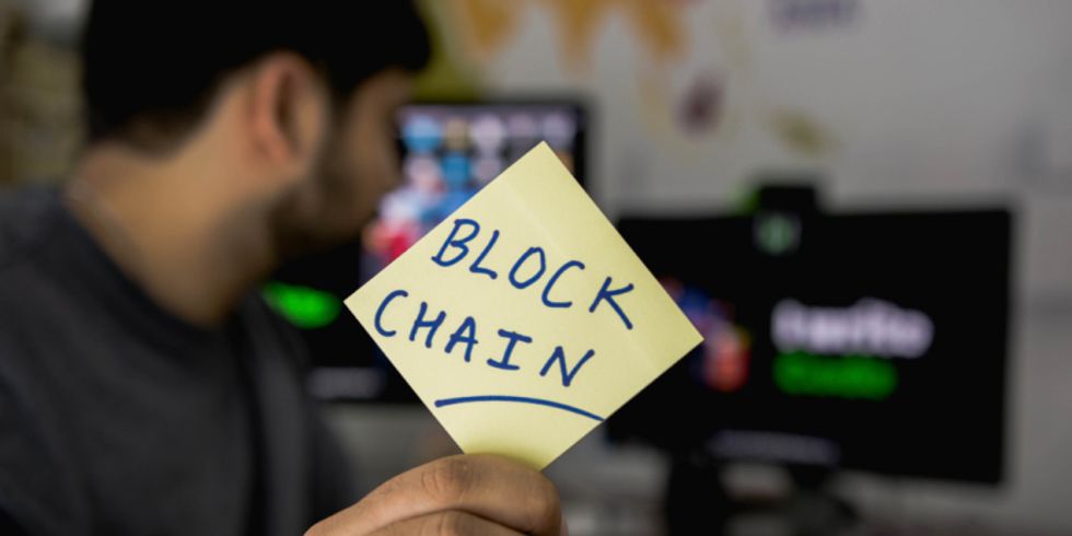 Mann hält Post-it mit dem Wort Blockchain in die Kamera