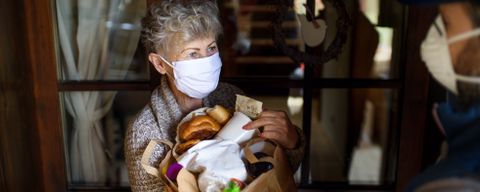 Kurier bringt Seniorin mit Mundschutz Einkäufe