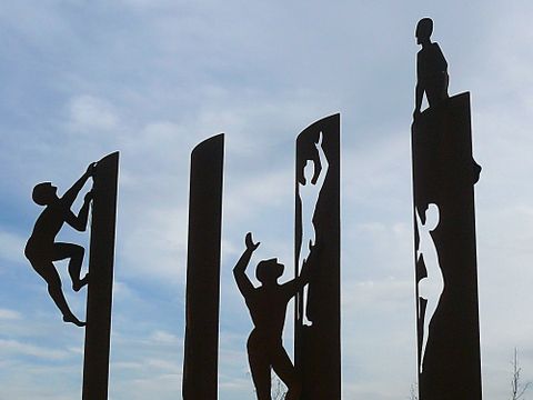 Bildvergrößerung: Ein Denkmal aus 4 Säulen an denen zweidimensionale Menschen klettern.