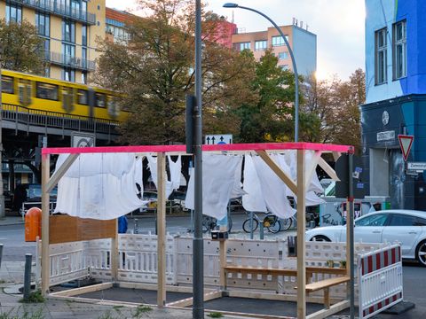 Bildvergrößerung: ein Holzgestell an einer Straßenkante an dem an Wäscheleinen weiße Kleidungsstücke aufgehängt sind