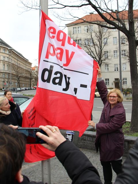 Bildvergrößerung: Frau hälz eine große rote Fahne mit der Schrift: Equal Pay Day
