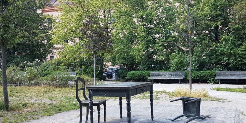 Denkmal "Der geschlossene Raum" auf dem Koppenplatz: Ein Tisch. Zwei Stühle. Ein Stuhl liegt auf der Rückenlehne.